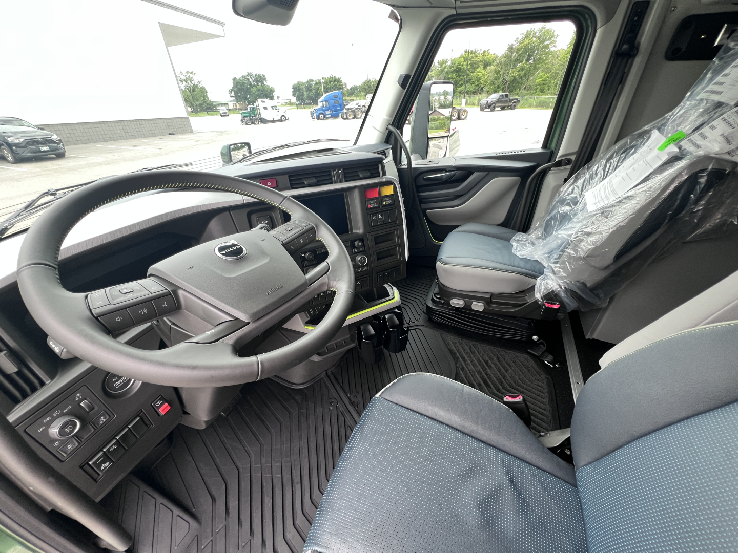 Volvo VNL64T860 truck cab interior showing steering wheel, dashboard, and driver seat with plastic-covered passenger seat.