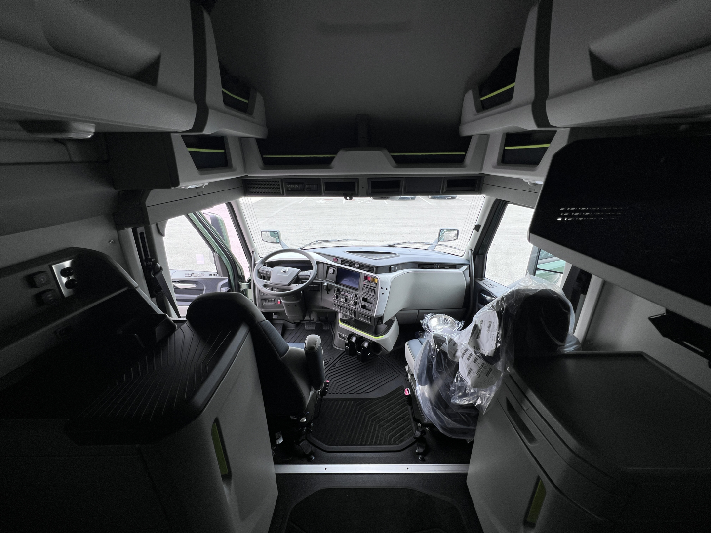 Cab interior of a new Volvo VNL64T860 sleeper cab showing dashboard, steering wheel, and overhead storage in view from between seats.