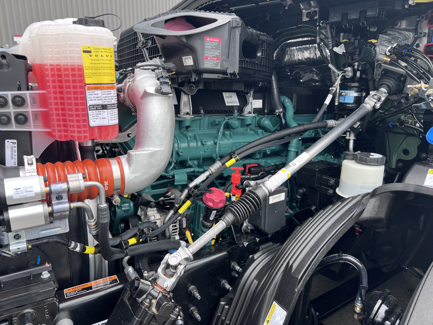 Volvo VNL64T860 engine bay showing coolant reservoir, turbo intercooler piping, and diesel engine with various hoses and fittings.