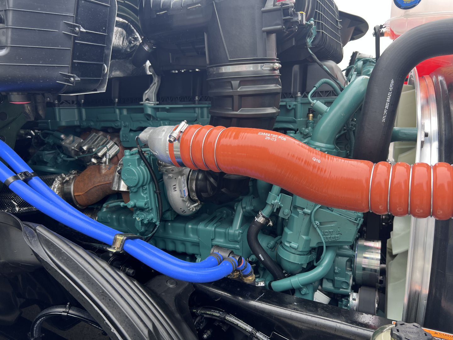 Volvo VNL64T860 engine bay showing orange turbo intercooler hose and green engine block with blue hoses and black plastic components.