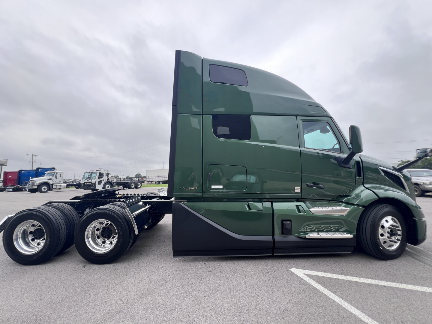 Volvo VNL64T860 truck side view showing green sleeper cab and wheel set with chrome fuel tanks and side steps.