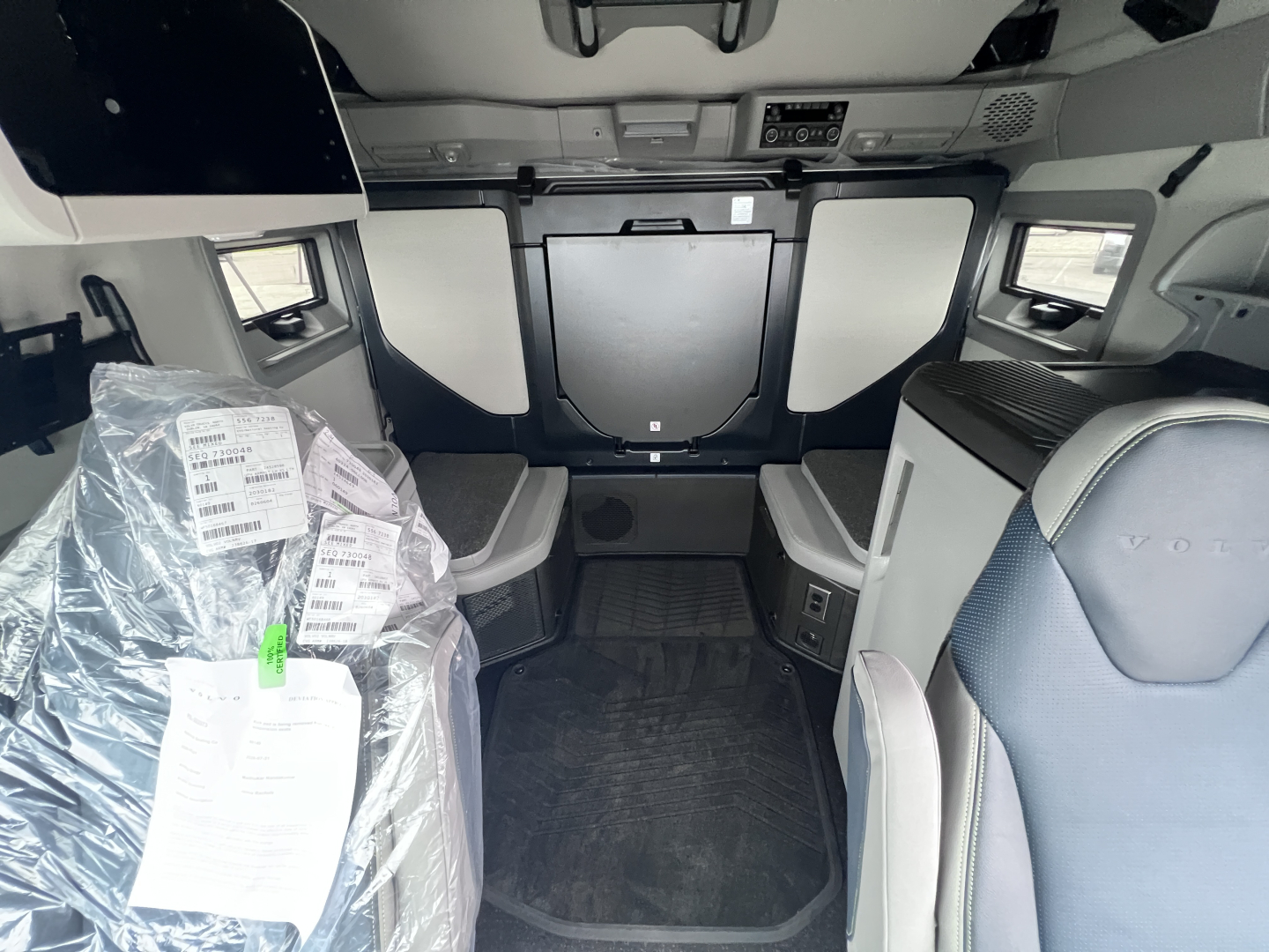 Volvo VNL64T860 sleeper cab interior with front cabin area, seats, and storage compartments visible; plastic-wrapped item on left, dashboard controls overhead panel.