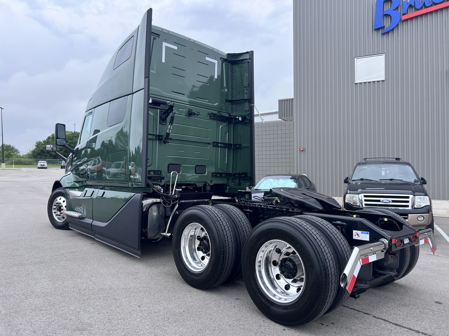 Volvo truck cab and chassis showing rear axle and dual wheels, dark green sleeper, with yard and building in background.