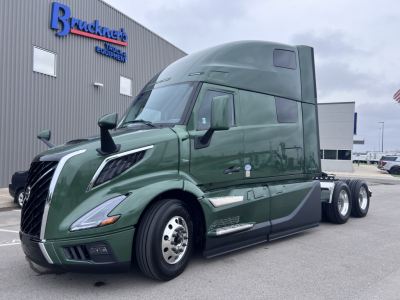 Green Volvo VNL64T860 cab with sleeper, front left view, showing curved hood, large side mirrors, and chrome wheel rims.