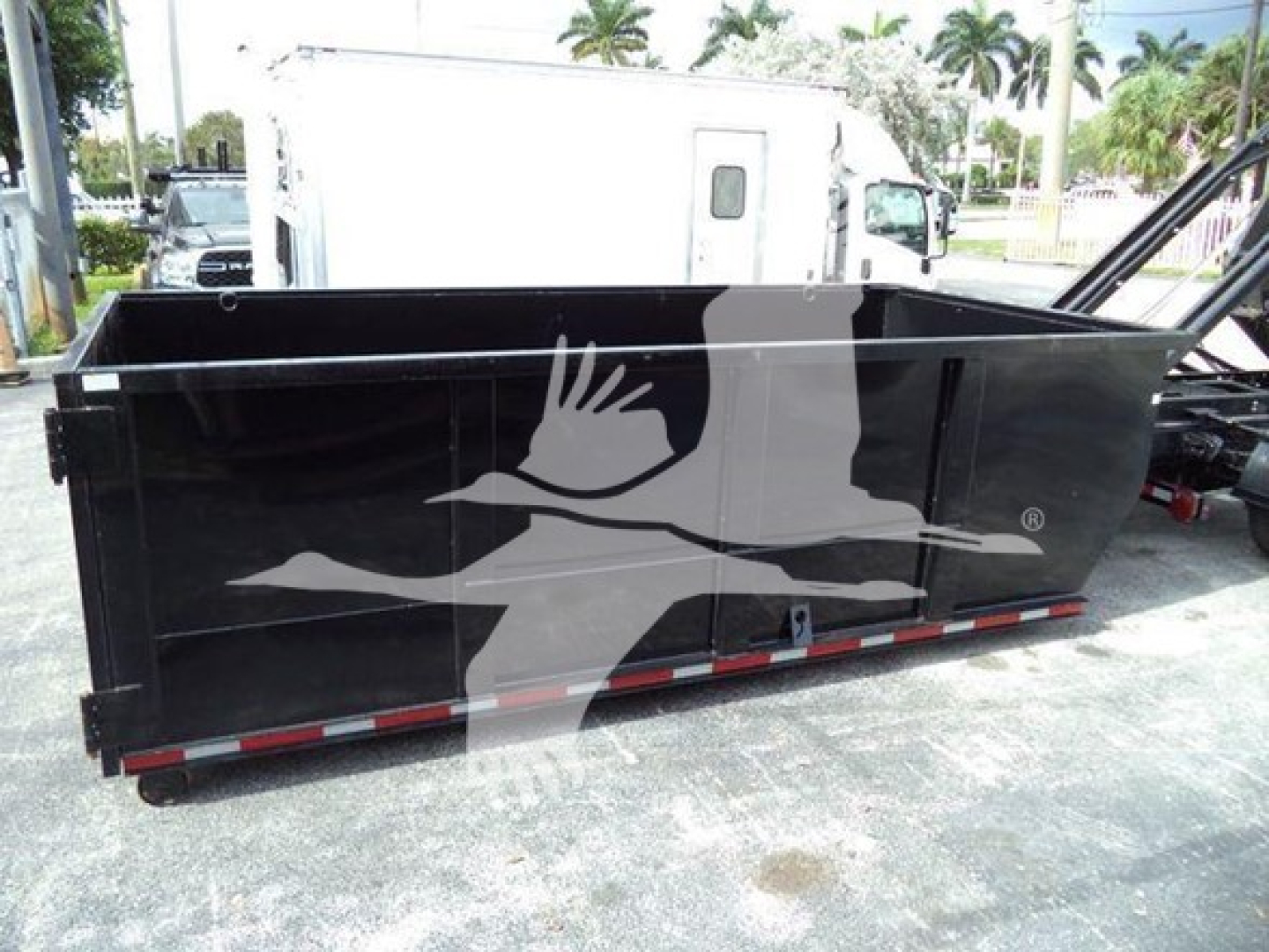 Truck bed container/dump body showing black exterior with white bird logo and red-and-white reflective strip along bottom edge.