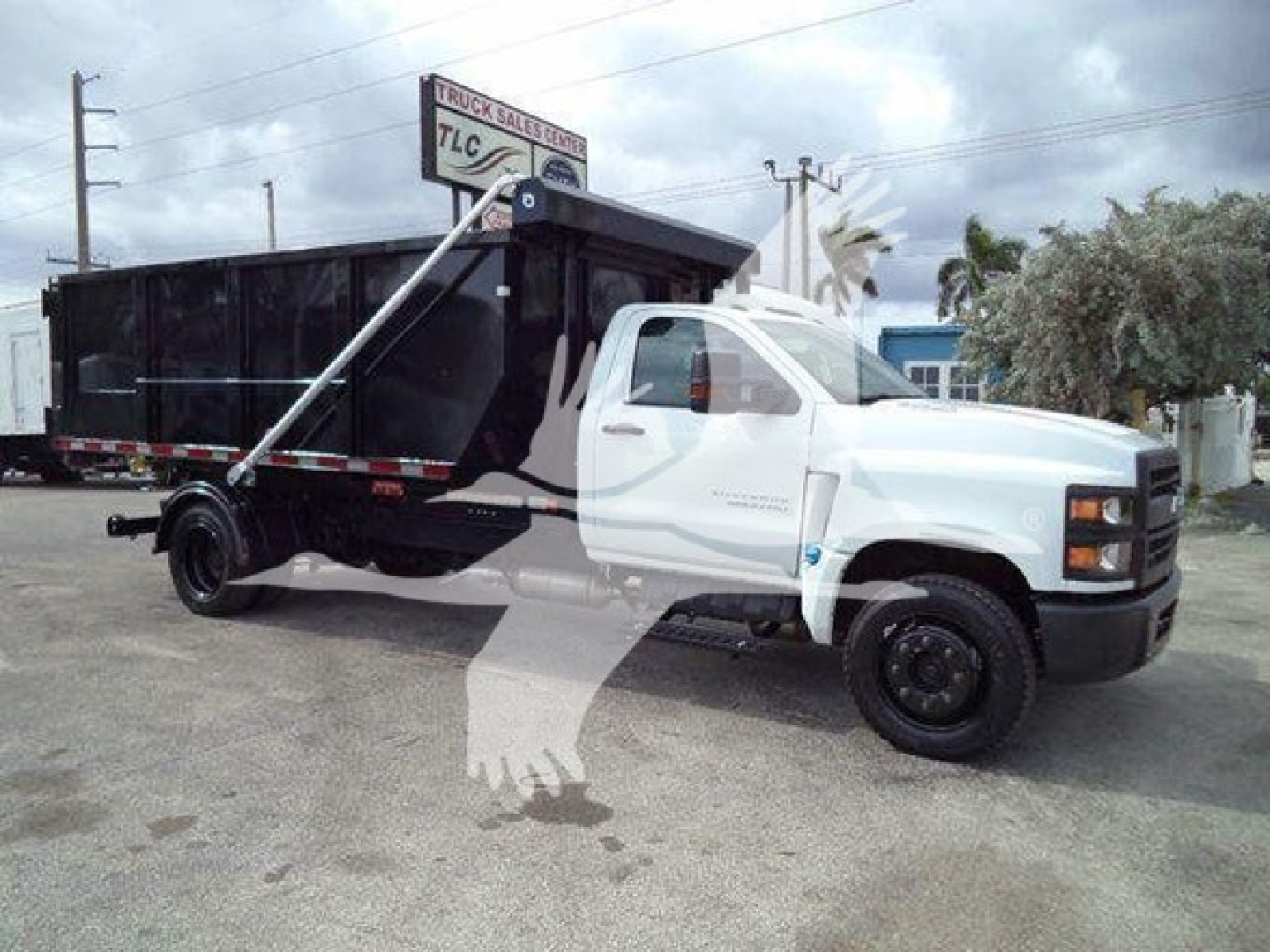 Medium-duty Chevrolet Silverado 6500HD roll-off truck with black dump body and white cab, side hydraulic arm raised, diesel engine vehicle.