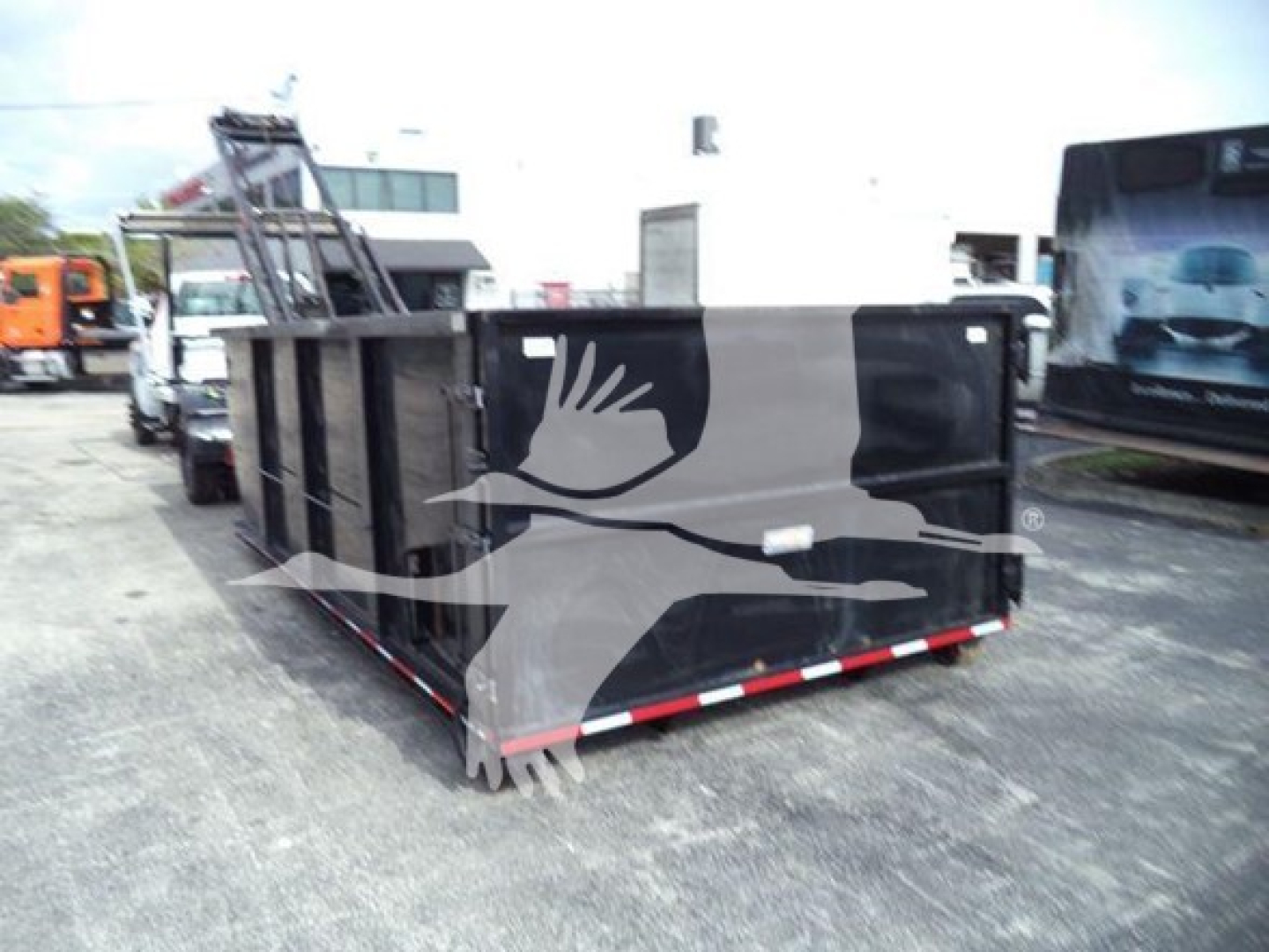Truck bed or container in a lot with a large graphic of a bird in flight on the side. The surface is black with gray panels, red-and-white reflective tape along the bottom edge. No visible text readable.