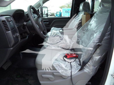Interior of a new 2023 Chevrolet Silverado 6500HD cab with plastic seat covers and a red handheld device on the passenger seat; steering wheel and dashboard visible.