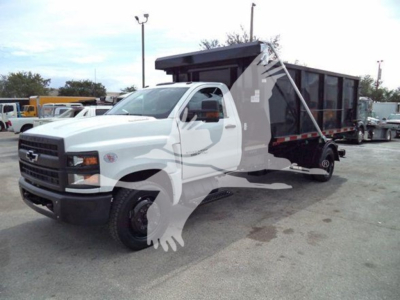 Truck shows a white 2023 Chevrolet Silverado 6500HD dump bed/rolloff with extended cab on a lot; front grille with Chevrolet emblem, side view reveals large equipment body on chassis.