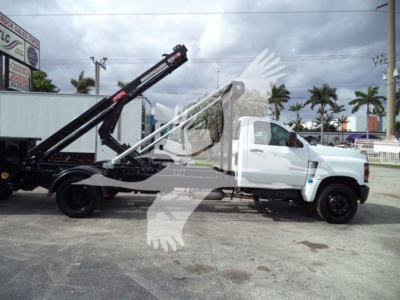 Truck with a long black loading arm on a white Chevrolet Silverado 6500HD chassis, side view, flatbed with roll-off hoist system.