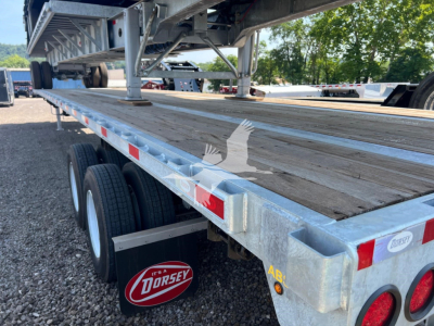 Flatbed trailer bed with wooden deck and dual rear axles, aluminum frame, Dorsey branding mudflap, red reflectors, and VIN/stock tags visible on the side.