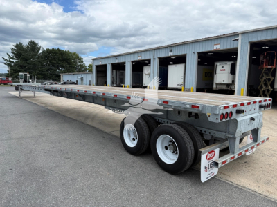 Flatbed trailer viewed side-on with extendable steel frame and dual rear axles, DOT lights, and reflective tape; VIN/stock not visible; Dorsey Extendable trailer in a yard with a building in the background.