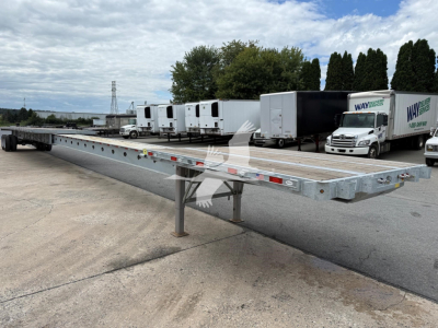 Flatbed trailer in an outdoor lot showing extendable trailer deck with dual landing gears and multiple white trailers in the background.