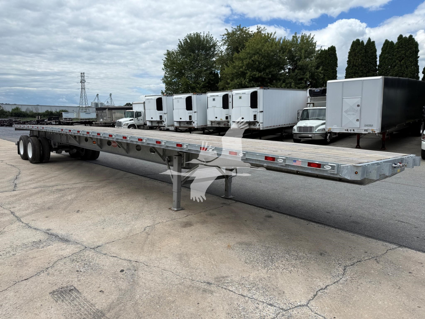 Flatbed trailer with gooseneck style frame and multiple refrigerated units in background.