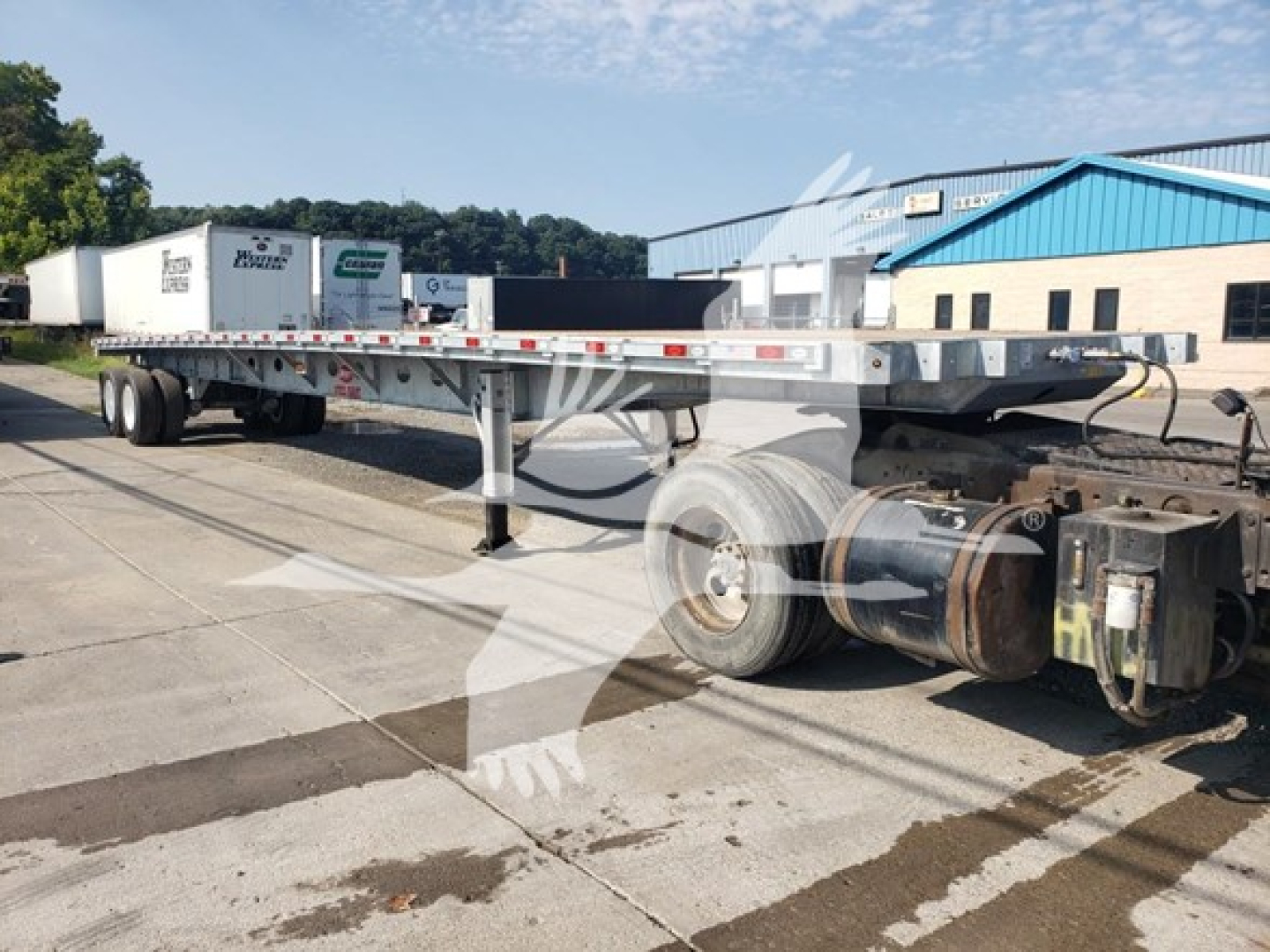 Flatbed trailer chassis and cab with long aluminum deck and dual rear axles, showing wheels, suspension, and hitch; no readable brand text on the visible portion.