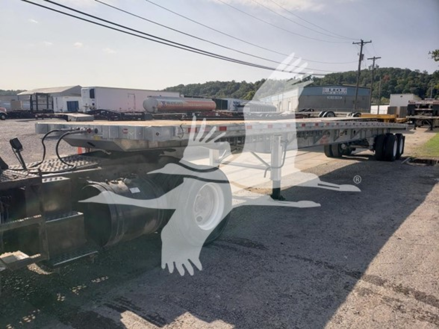 Dorsey galvanized flatbed trailer in-service showing long flat deck and dual rear axles with tires; faint reflection of dealership logo over image.