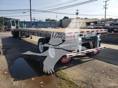 Flatbed trailer showing galvanized deck with rear and side reflectors, brand sticker, and dual rear lights; rear bumper crossbars visible.
