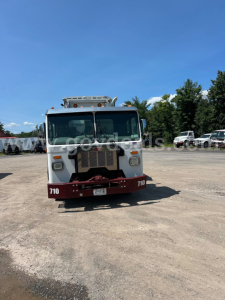 Peterbilt garbage truck front view showing white cab, red bumper with '710' numbers, and grille, in a lot with other trucks.