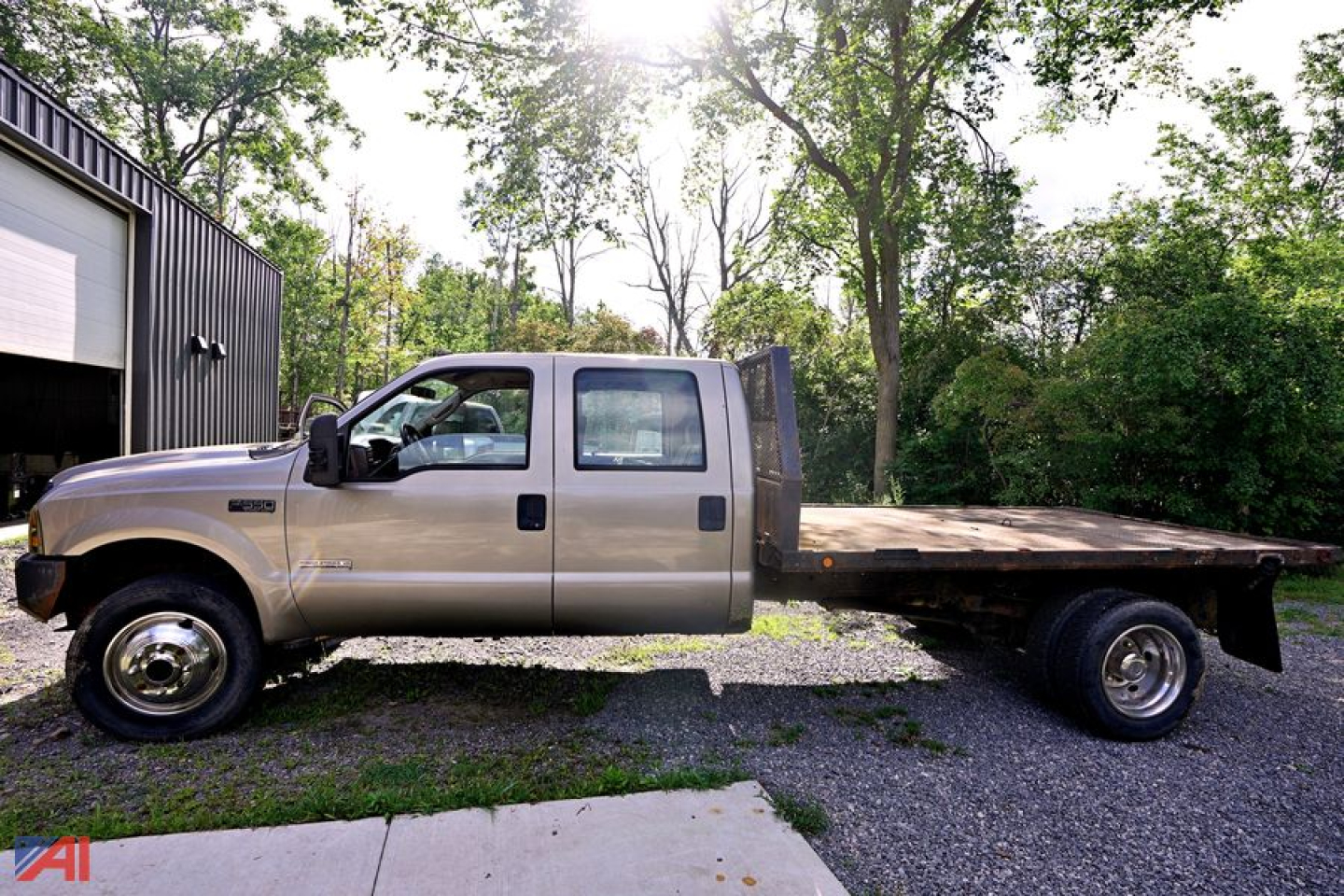 Vehicle side view of a beige 2004 Ford F-550 stake bed truck with extended cab, flatbed rear, dual rear wheels, and tree-lined background.