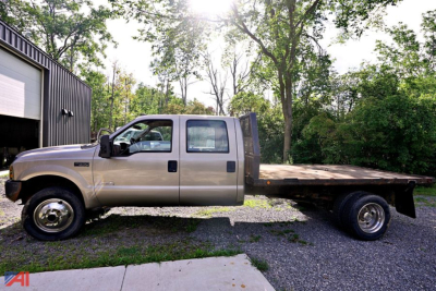 Vehicle side view of a beige 2004 Ford F-550 stake bed truck with extended cab, flatbed rear, dual rear wheels, and tree-lined background.