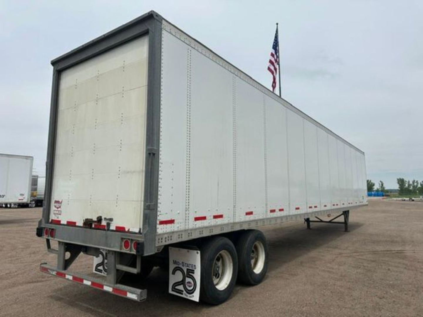 Trailer side view showing a long white Wabash trailer with dual rear axles and rear lights, no visible branding.