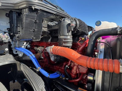 Mack PR64T engine bay showing red diesel engine with blue and orange hoses and intake components.