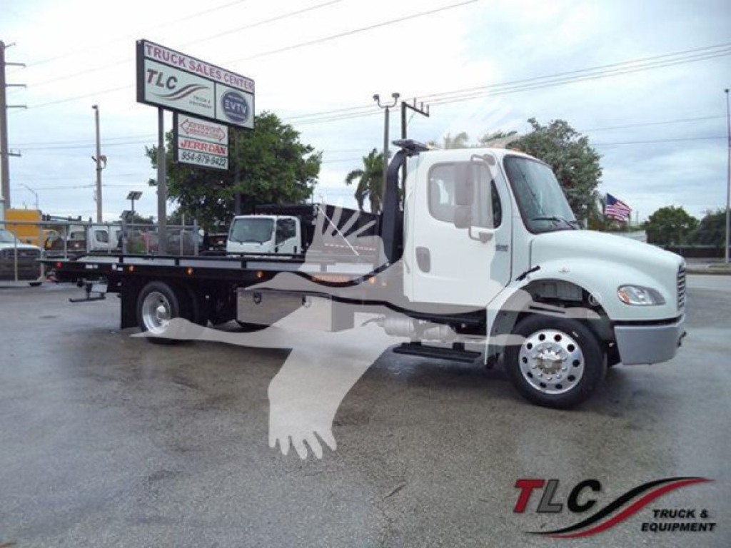 Freightliner M2 106 rollback truck side profile in dealership lot, white cab, flatbed body, dealership signage in background.