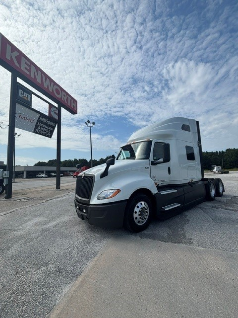 Truck showing a white 2021 International LT625 sleeper cab in a dealership lot with Kenworth sign in background.