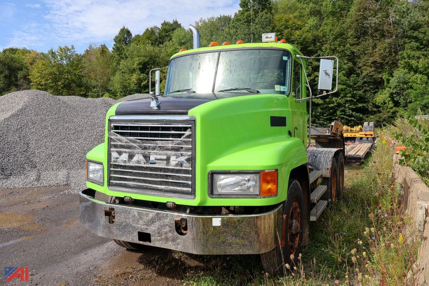 Green Mack CH613 tractor daycab truck front view with chrome bumper and grille, flatbed behind, outdoor lot.
