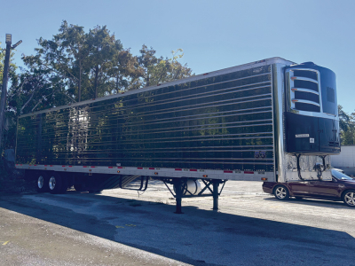 Reefer trailer with stainless steel exterior and black finish, 5-axle wheels, front refrigeration unit, dock height legs, side reflectors.