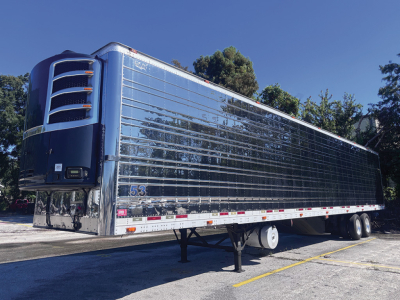 Reefer trailer with stainless steel corrugated sides and teal-blue refrigeration unit at the front, parked on a lot.