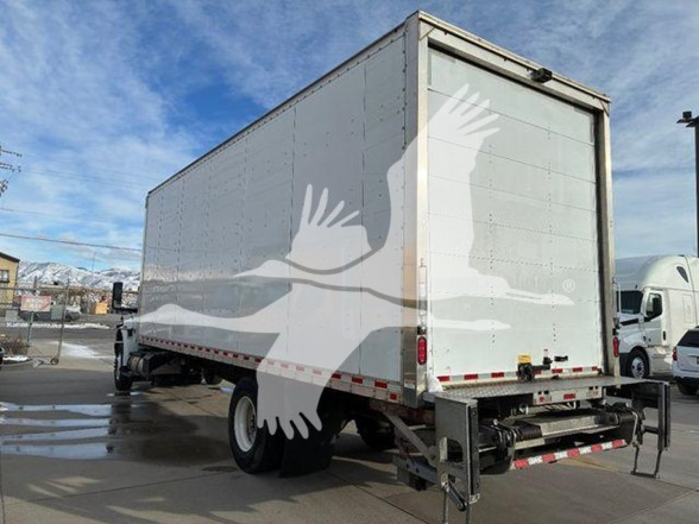 Box truck rear and side view showing a large white cargo box on a truck trailer with a roll-up door and rear underride guard.