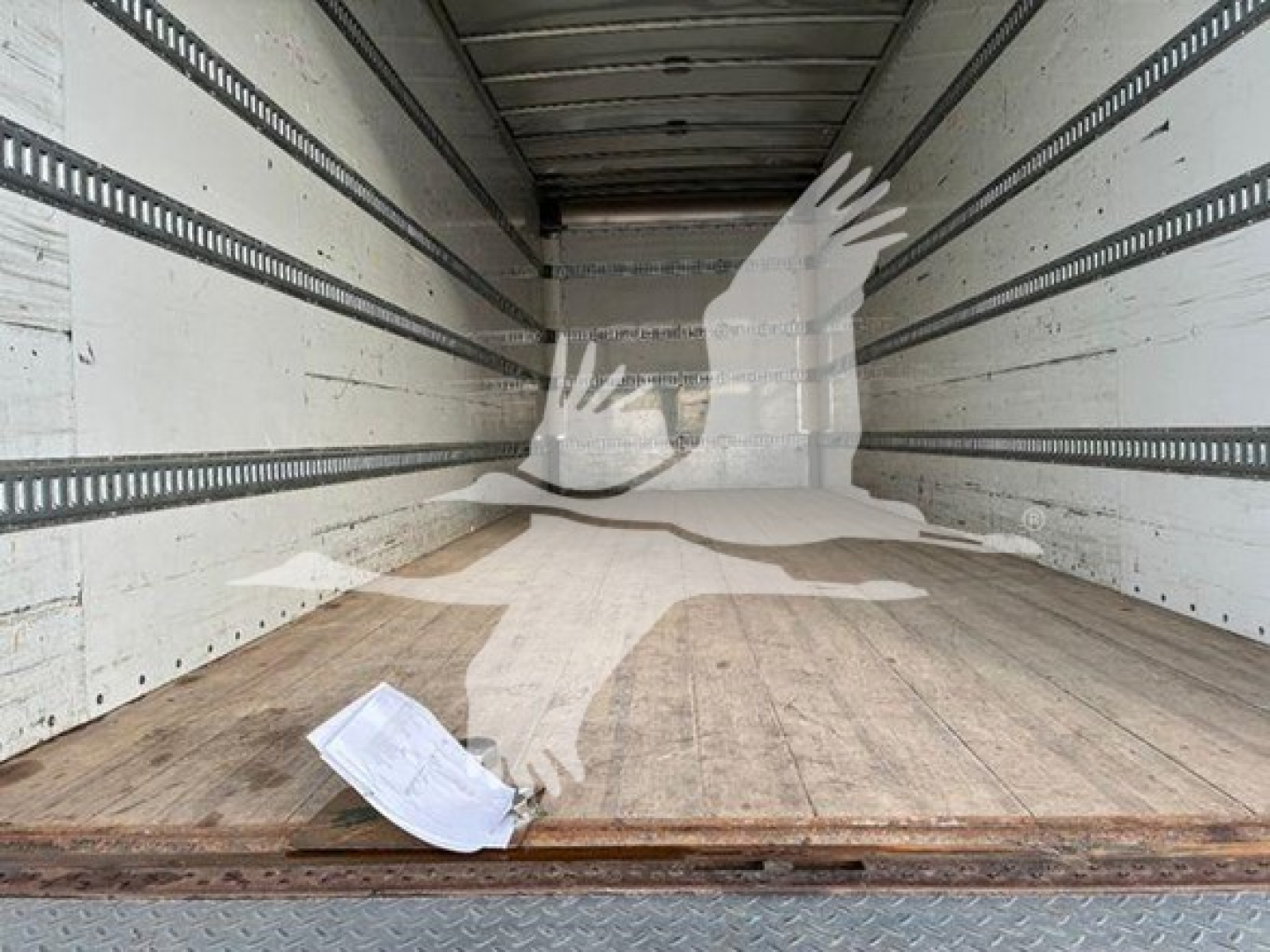 Trailer interior showing empty box truck cargo area with wooden floor and sidewall rails; a crumpled paper lies near the door.