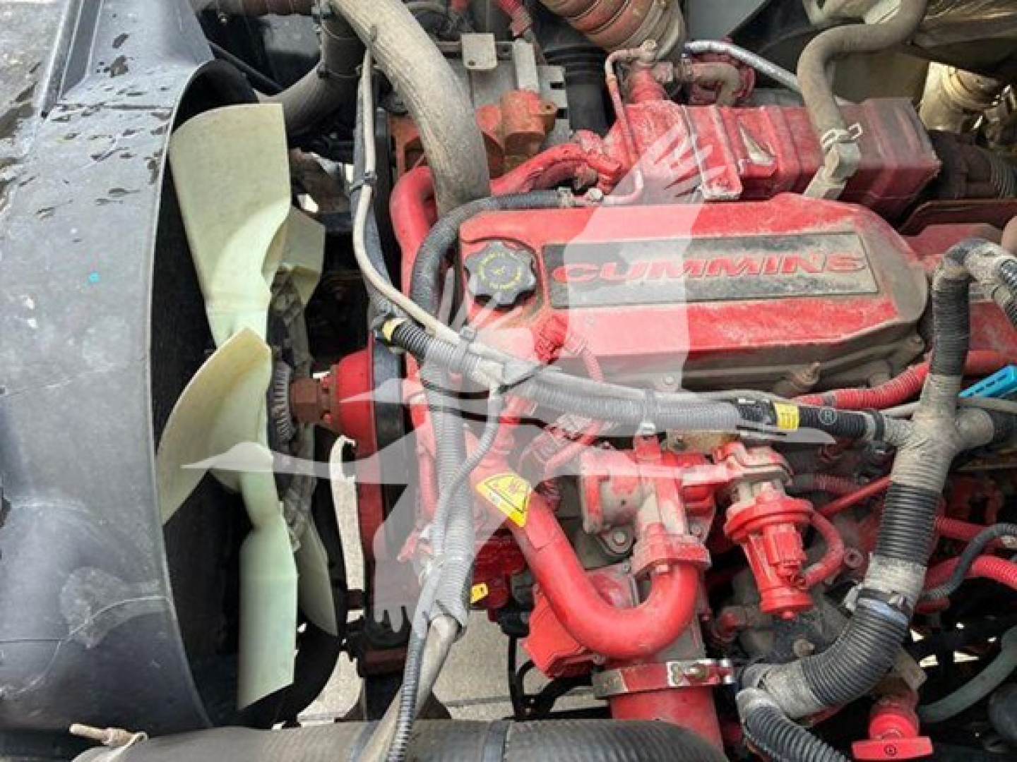 Engine bay showing a red Cummins diesel engine with radiator fan and various hoses and wiring.