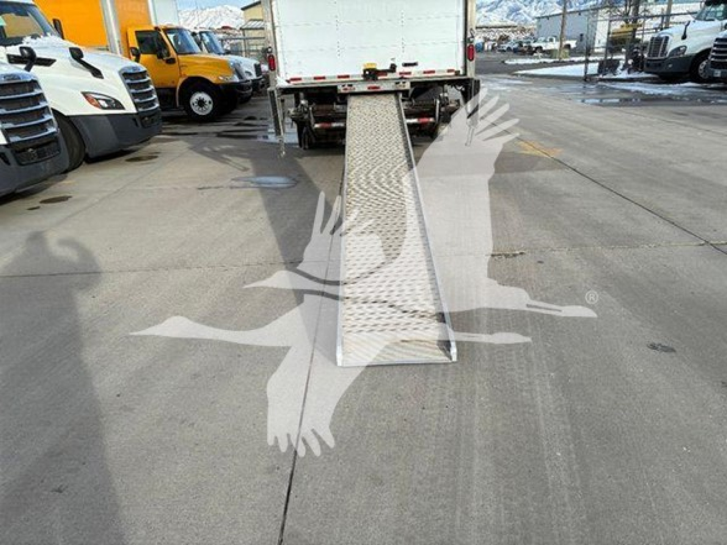 Truck with side ramp extended in a parking lot, rear view showing cargo area and metal diamond-plate ramp.