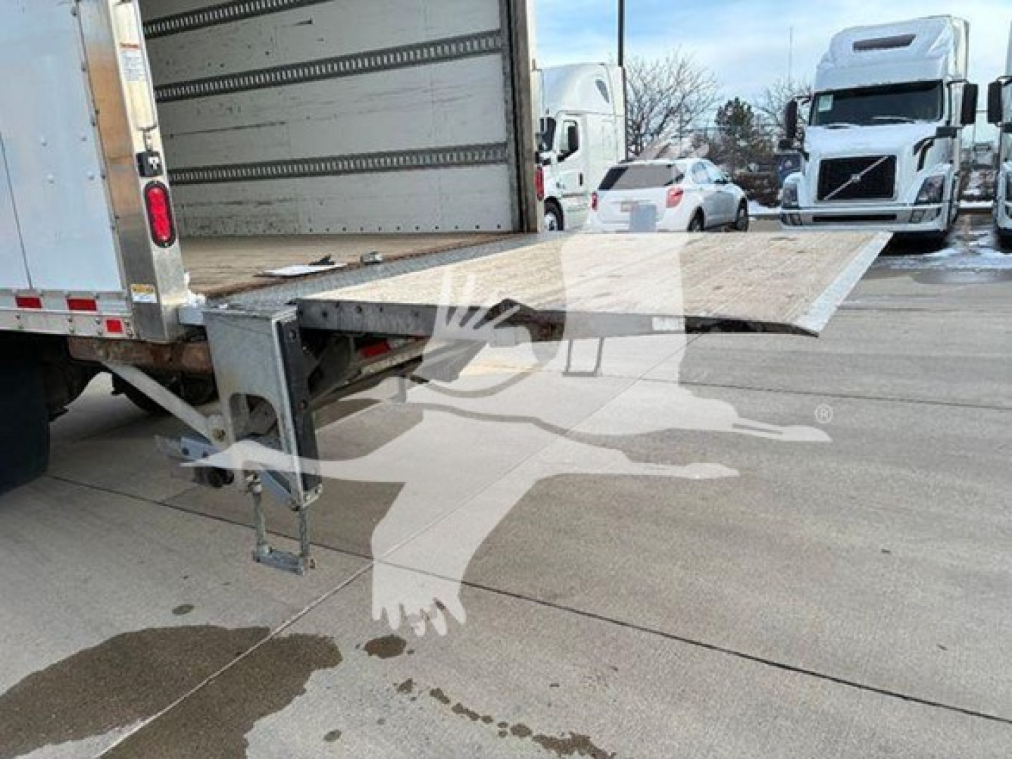 Truck bed with hydraulic ramp extended from a box truck trailer, showing loading ramp and rear of cargo area.