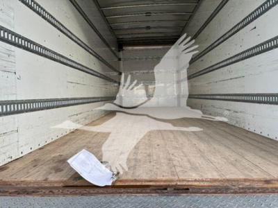 Trailer interior showing empty box truck cargo area with wooden floor and sidewall rails; a crumpled paper lies near the door.