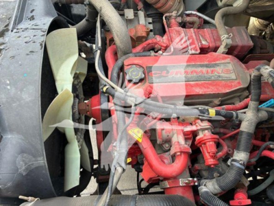 Engine bay showing a red Cummins diesel engine with radiator fan and various hoses and wiring.