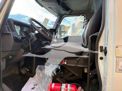 Cab view of a 2021 International MV box truck showing steering wheel, dashboard, driver seat, and pedals; VIN tag visible on door frame; general interior details.