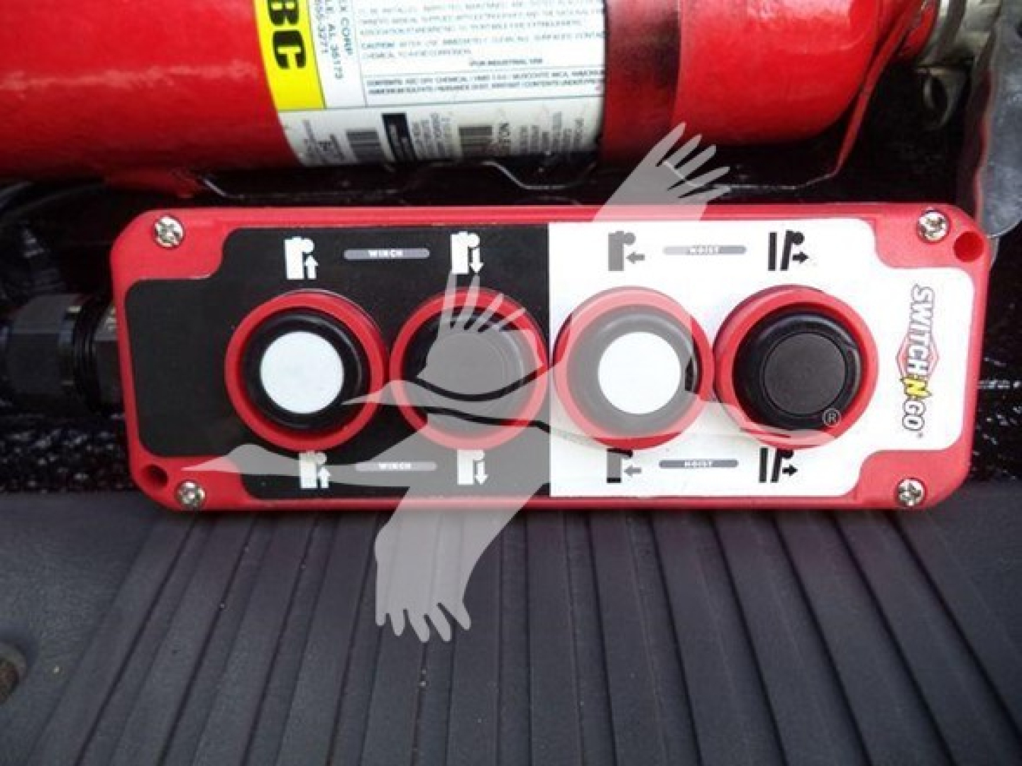 Control panel with three circular knobs on red unit; labels and arrows visible; part of a hydraulic system in a truck bed.