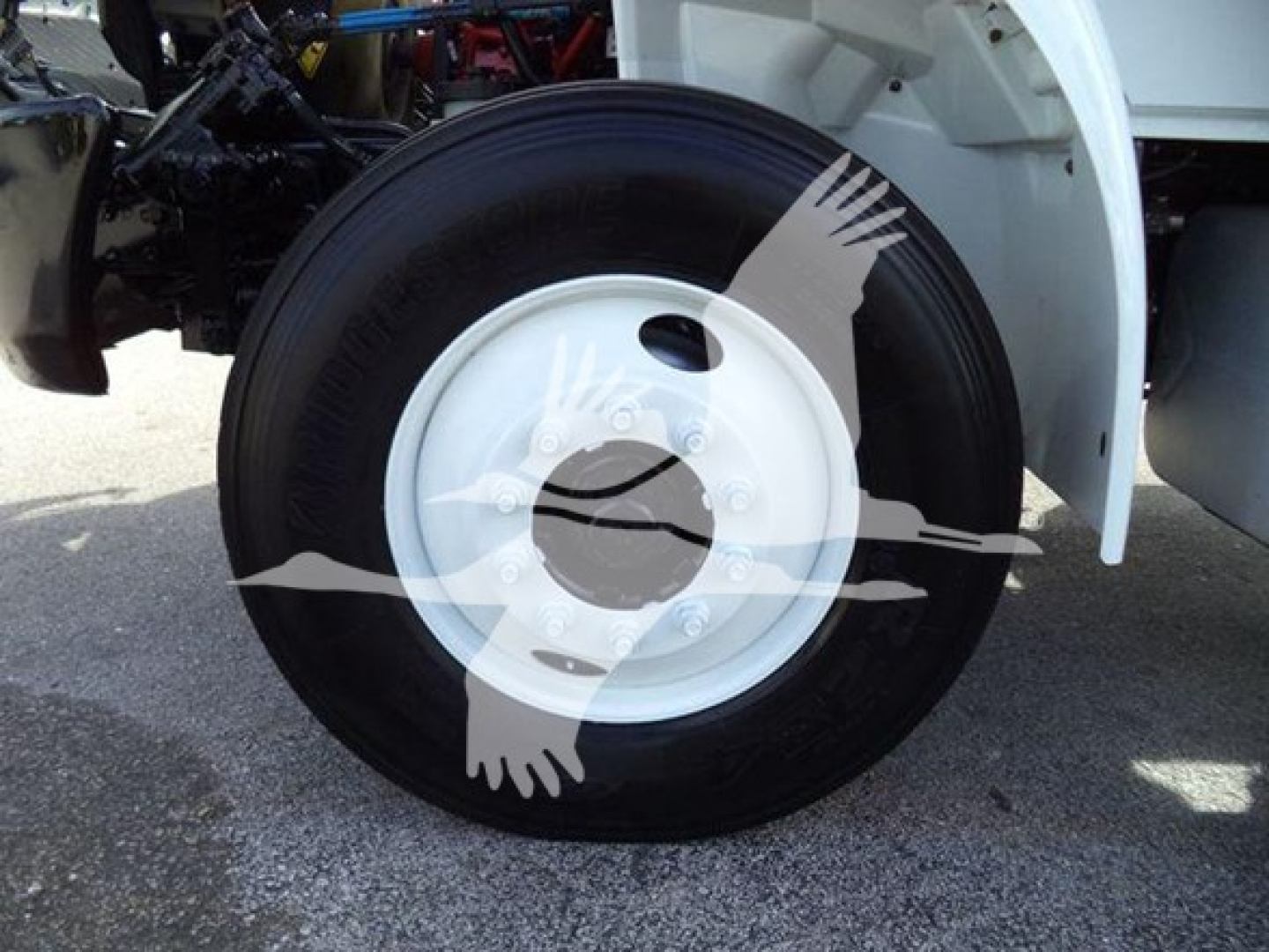 Front wheel of a 2019 International Durastar 4300 roll-off truck showing black tire with white steel wheel and wheel cover; part of the truck fender visible.