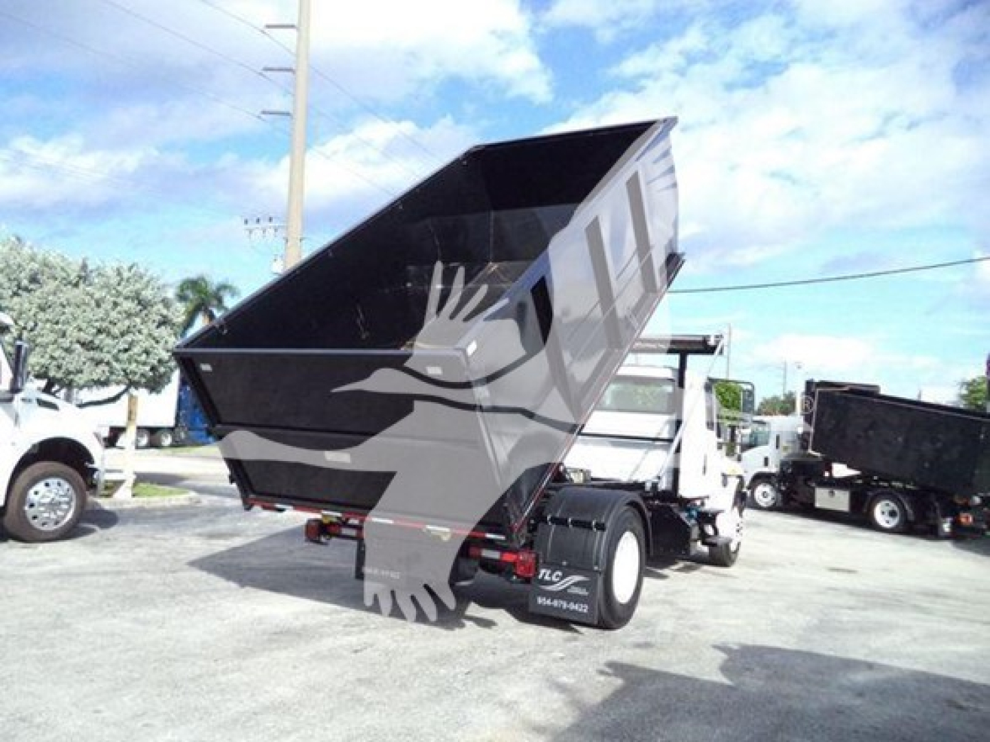Dump truck in a lot with raised bed and rear hydraulics, International Durastar 4300 rolloff bed visible, black and gray color, company lot background.