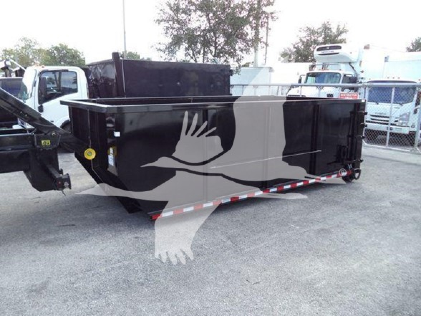 Dump trailer with roll-off container attached showing black metal bed and hitch in a lot