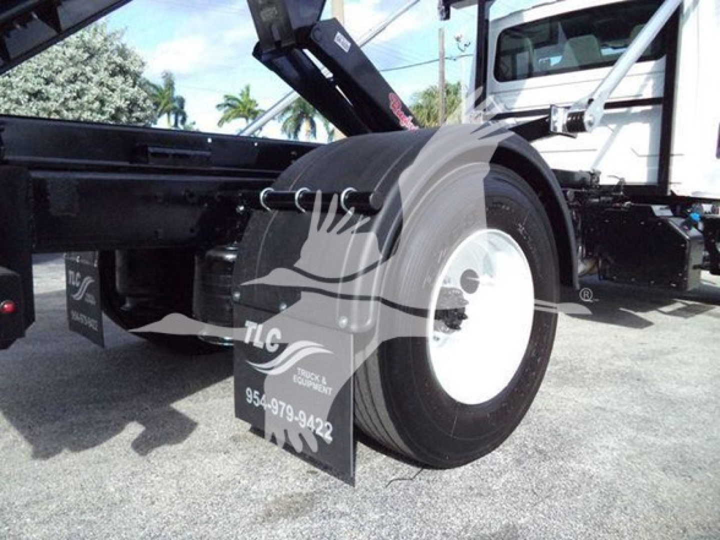 Truck chassis showing rear wheel and hitch area of a 2019 International Durastar 4300 roll-off truck; visible components include wheel, mud flaps with TLC logo, and chassis frame.