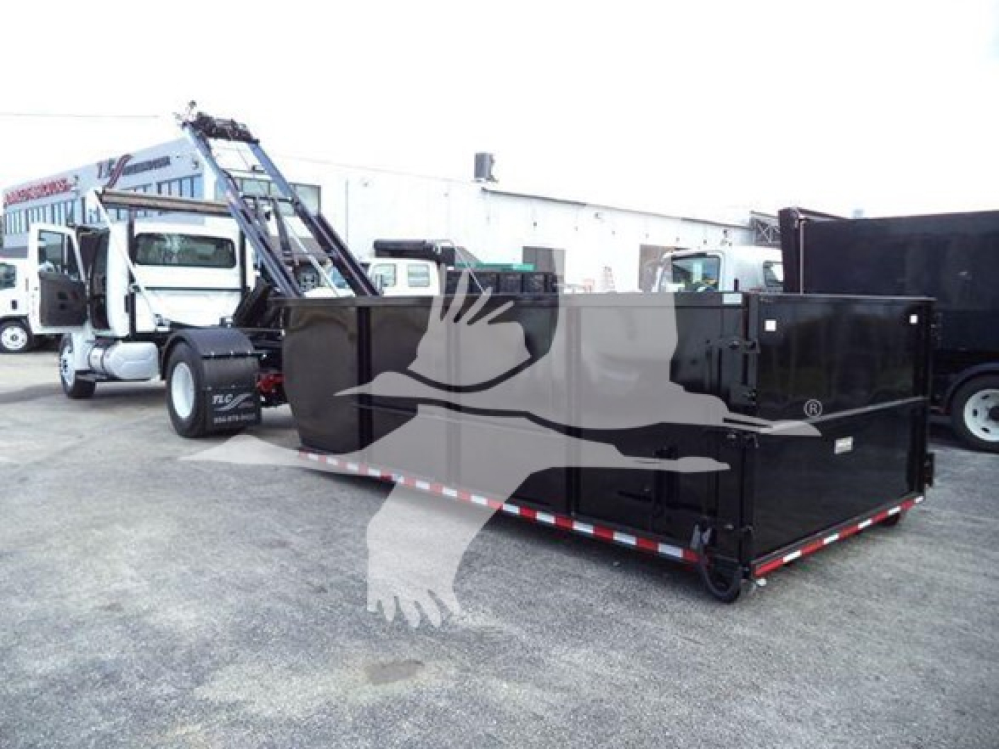 Dump truck with a large black roll-off container attached to a white International truck, loading area visible.