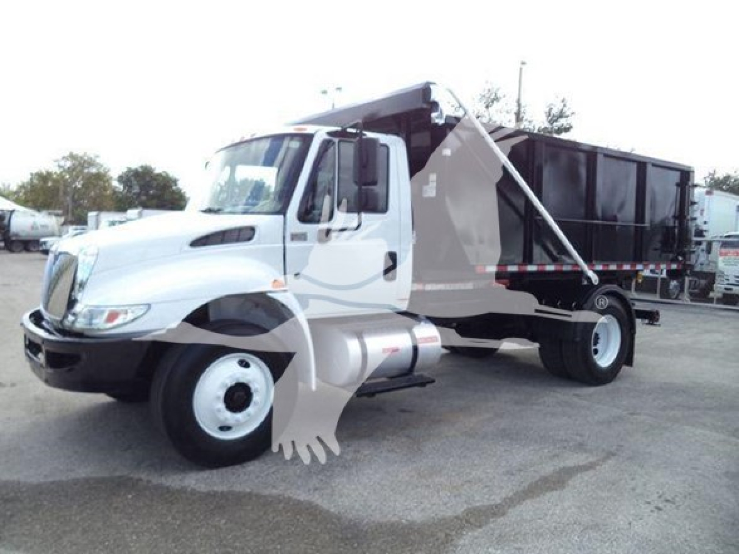 Truck in-service International Durastar 4300 roll-off truck with dump bed, cab interior not visible, side view showing front wheel and rear container.
