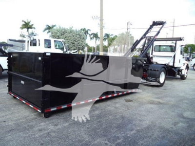 Truck bed showing roll-off container attached to a white International Durastar 4300, with stock yard in background.