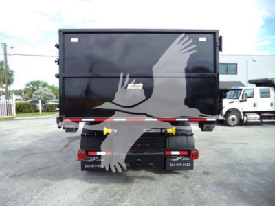 Back view of a 2019 International Durastar roll-off truck with a black dump body and white graphics of hands. Visible text includes contact numbers on bumper, and small signs on the rear.
