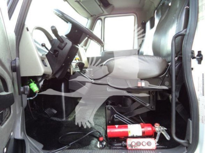 Interior of a 2019 International Durastar 4300 cab showing steering wheel, dashboard, driver seat, and a red fire extinguisher mounted under the dash area.