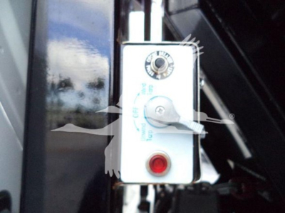 Control panel with circular dial and red push button on a white metal box; partial blue label text around the dial.